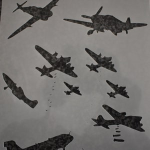 Könnte beinhalten: Eine Schablonenfolie mit dem Text "GET STENCILLED" oben. Die Folie zeigt mehrere Silhouetten von Flugzeugen, darunter ein Bomber, der Bomben abwirft.