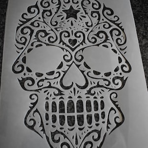 Può includere: Uno stencil bianco con un disegno nero di un teschio di zucchero con dettagli intricati. Lo stencil dice "GET STENCILLED" in alto.