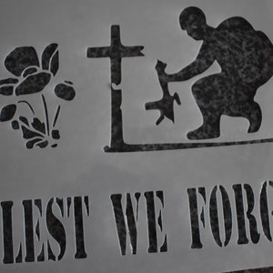 May include: A black and white stencil with a poppy flower, a cross, a soldier kneeling and a dog, and the text "Lest We Forget".