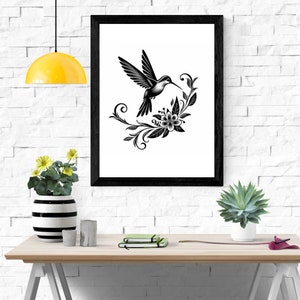 K&ouml;nnte beinhalten: Schwarz-wei&szlig;-Illustration eines Kolibris im Flug mit einem floralen Design dahinter. Das Bild ist in einem schwarzen Rahmen gerahmt und h&auml;ngt an einer wei&szlig;en Backsteinwand.