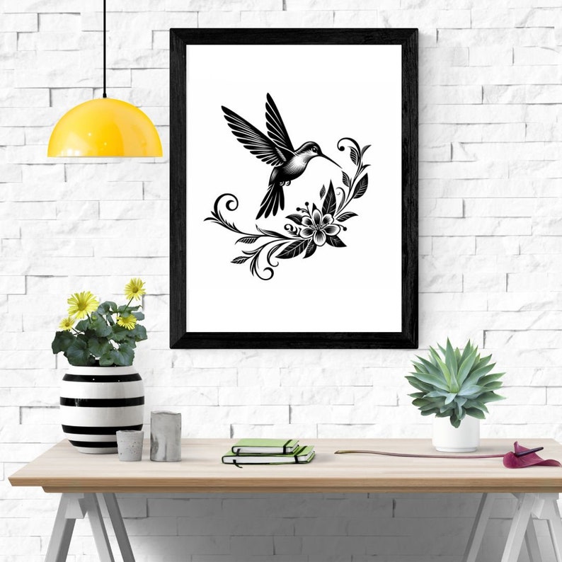 K&ouml;nnte beinhalten: Schwarz-wei&szlig;-Illustration eines Kolibris im Flug mit einem floralen Design dahinter. Das Bild ist in einem schwarzen Rahmen gerahmt und h&auml;ngt an einer wei&szlig;en Backsteinwand.
