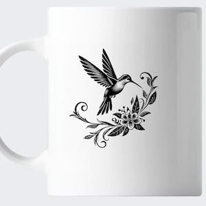 K&ouml;nnte beinhalten: Wei&szlig;e Keramiktasse mit einer schwarzen Silhouette eines Kolibris, der &uuml;ber einem floralen Design schwebt.