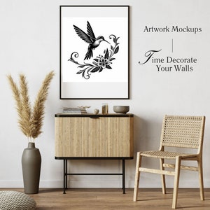 K&ouml;nnte beinhalten: Schwarzwei&szlig;-Illustration eines Kolibris mit Blumen in einem schwarzen Rahmen, der an einer wei&szlig;en Wand &uuml;ber einem Holzschr&auml;nkchen mit einem Korbstuhl rechts h&auml;ngt. Der Text "Artwork Mockups" und "Time Decorate Your Walls" ist in der oberen rechten Ecke des Bildes sichtbar.