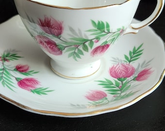 May include: A white teacup and saucer with a gold trim and a floral pattern of pink flowers and green leaves.