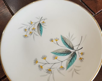May include: A white ceramic bowl with a gold rim and a floral design featuring teal and gray leaves and yellow flowers.