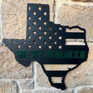 May include: Black metal Texas state outline with the American flag design and a green personalized nameplate that reads "SMITH".