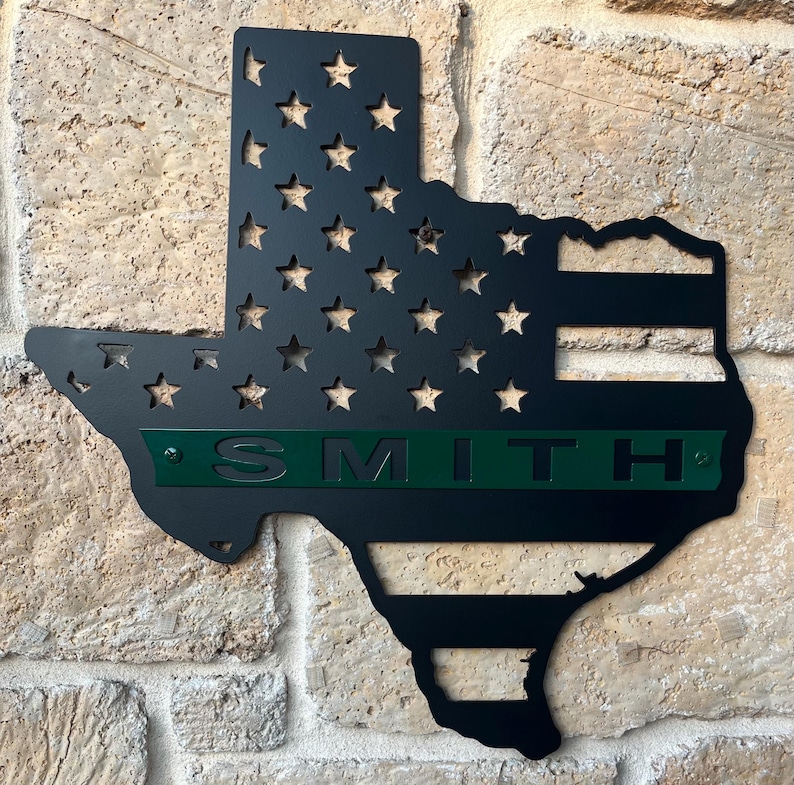May include: Black metal Texas state outline with the American flag design and a green personalized nameplate that reads "SMITH".