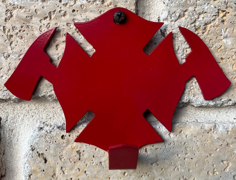 May include: Red metal firefighter's axe hook, shaped like a traditional fire department symbol. The hook is mounted on a wall.