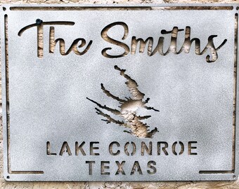 May include: A metal sign with the text "The Smiths" in a cursive font. Below the name is a silhouette of a lake and the text "Lake Conroe Texas".