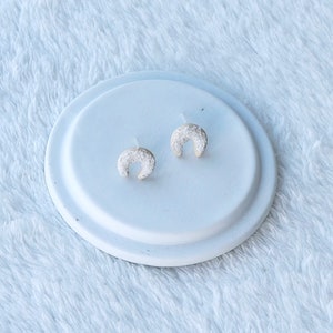 May include: A pair of silver horseshoe-shaped earrings with a textured, sparkly finish.