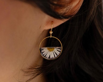 May include: Gold-tone hoop earrings with a half-circle design. Each earring features a preserved white daisy flower encased in clear resin. The earrings have a delicate, nature-inspired aesthetic.