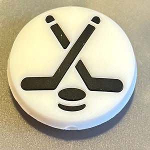 May include: White hockey puck with a black hockey stick and puck design.