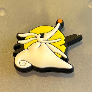 May include: A black and white rubber charm of Jack Skellington from the Nightmare Before Christmas movie. The charm features Jack Skellington with his signature stitched mouth and a yellow moon behind him.