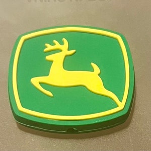 May include: A green and yellow rubber patch with a stylized deer silhouette. The deer is facing right and has a yellow outline.