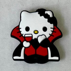 May include: A white Hello Kitty character dressed as a vampire, wearing a red cape and holding a glass of red liquid.