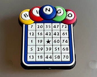 May include: A blue and white bingo card with a black border and a star in the centre. The card has numbers 7, 20, 35, 47, 72, 12, 16, 42, 42, 61, 1, 19, 60, 74, 5, 29, 39, 51, 68, 13, 18, 44, 58, 70. The card is topped with a colourful B-I-N-G-O sign.