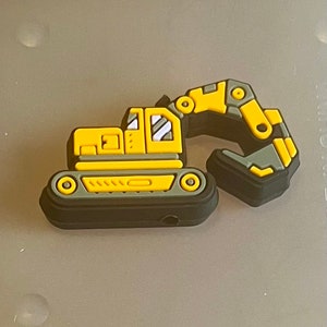May include: A yellow and gray excavator charm. The charm features a detailed design of a construction vehicle with a movable arm and a track base. The excavator is a vibrant yellow with gray accents and black trim.