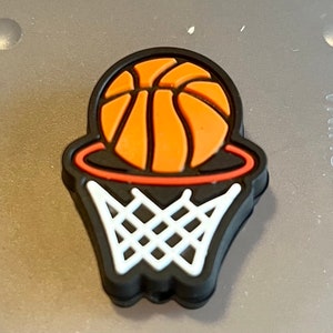May include: A black basketball hoop with an orange basketball going through the net. The hoop is outlined in red.