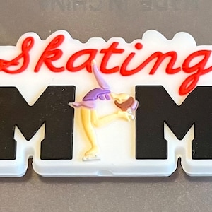 May include: White plastic charm with the words "Skating Mom" in red and black lettering. A cartoon figure of a figure skater is in the middle of the charm.