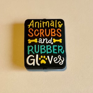 May include: A black rectangular charm with the words "Animals, Scrubs, and Rubber Gloves" in colorful, raised lettering. The design includes bone and paw print graphics, suitable for veterinary professionals or animal lovers.