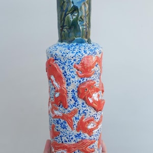 May include: A ceramic vase with a blue and white speckled glaze. The vase is decorated with orange fish and a crab.