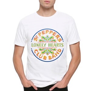May include: White t-shirt featuring a colourful graphic of the Beatles' "Sgt. Pepper's Lonely Hearts Club Band" album cover.