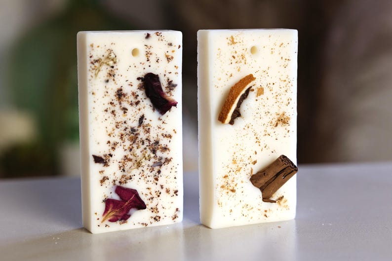 K&ouml;nnte beinhalten: Zwei wei&szlig;e Wachsschmelzen, eine mit getrockneten Blumen und die andere mit getrockneten Zitrusfr&uuml;chten und Zimt. Beide haben ein Loch zum Aufh&auml;ngen.