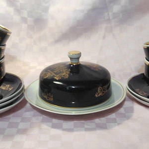 May include: A set of six black and gold teacups and saucers with a matching black and gold lidded butter dish. The cups and saucers have a gold floral design on a black background.