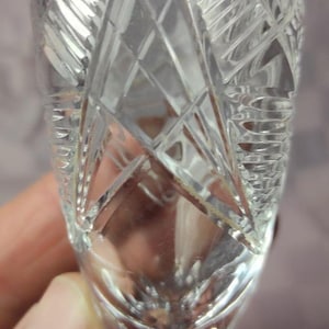 Puede incluir: Copa de vino de cristal transparente con intrincados patrones de corte de diamante y abanico. El tallo es delgado y la copa es sostenida por una mano. La copa está diseñada para servir vino.