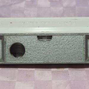 Può includere: Una livella rettangolare con parte superiore bianca e base in metallo grigio. La base presenta un foro circolare e il testo "УБ-250" e "ЦЗ Р 50 К С футляром". Strumento per misurare l'allineamento orizzontale e verticale.