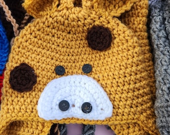 May include: A crocheted giraffe hat with brown spots and a white face. The hat has a long brim and a brown and black braided trim.