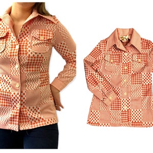Puede incluir: Una camisa de manga larga con botones y un diseño de patchwork con patrones geométricos naranja, blanco y negro. La camisa tiene un cuello puntiagudo y dos bolsillos de solapa.
