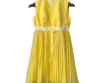 Könnte beinhalten: Ein gelbes, ärmelloses Kleid mit weißer Spitzenborte und einer gelben Schleife an der Taille. Das Kleid ist plissiert und hat einen hohen Ausschnitt.