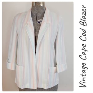 May include: A vintage striped white, pink and blue cape blazer. The blazer has a long, open front and long sleeves with turn-up cuffs. The blazer has two pockets on the front.