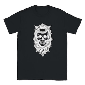Peut inclure: Un t-shirt noir à manches courtes avec une impression graphique blanche sur la poitrine. Le motif représente un crâne humain entrelacé d'un serpent, centré dans un cadre orné, pointu et décoratif avec des bords acérés et des accents en étoile.