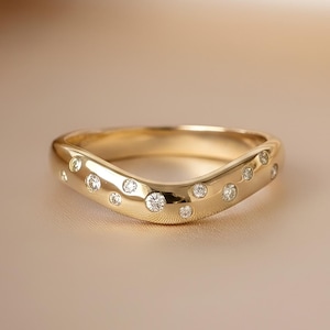 Peut inclure: Une bague dorée au design incurvé, sertie de plusieurs petites pierres précieuses transparentes. La bague a une finition lisse et polie et est présentée sur un fond neutre.