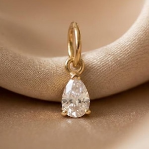 May include: A gold pendant featuring a single pear-shaped clear gemstone held by a small metal bail. The pendant is crafted from polished yellow gold and showcases a faceted stone that reflects light, suspended from a circular jump ring connector.