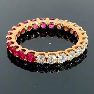 May include: A rose gold eternity ring with alternating red and clear gemstones. The ring features a continuous row of vibrant red rubies and sparkling clear diamonds, creating a striking contrast. The ring is displayed on a reflective black surface.