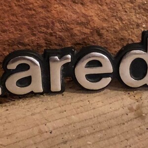 May include: A black and silver car emblem with the word "Laredo" in raised letters.