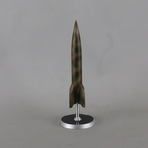 May include: A model of a rocket with a camouflage paint scheme on a silver stand. The rocket is pointed upwards.