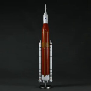 May include: A white and orange model rocket with a black and white NASA logo on the side. The rocket is on a black stand.
