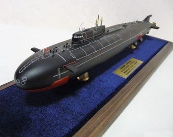 Pode incluir: Um modelo preto e vermelho de um submarino russo, "Severodvinsk", em um suporte de madeira com uma placa dourada.