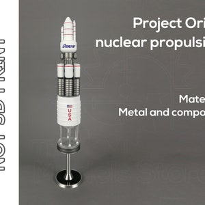 May include: A white and silver model of the Project Orion nuclear propulsion spacecraft. The model is labeled "Orion" and "USA". The text "Project Orion nuclear propulsion" and "Material: Metal and composite" are visible in the background.
