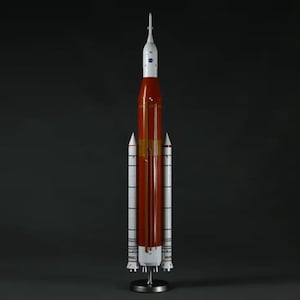 May include: A white and orange model rocket with a black and white NASA logo on the side. The rocket is on a black stand.