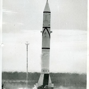 Może przedstawiać: Czarno-białe zdjęcie startującej rakiety. Rakieta jest cylindryczna z czarno-białymi akcentami i spiczastym wierzchołkiem. Słowa "CONFIDENTIAL SECURITY INFORMATION" są wydrukowane u góry i u dołu obrazu.