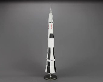 Pode incluir: Um modelo de foguete branco e preto com uma inscrição vermelha "USA" no lado. O foguete está em um suporte prateado.