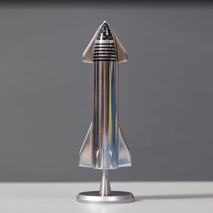 May include: A silver model of a rocket ship with a black and white design on the top. The rocket is on a silver stand.