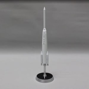 Może przedstawiać: Biały model rakiety z czarną podstawą i napisem "UNITED STATES" oraz "30" na boku.