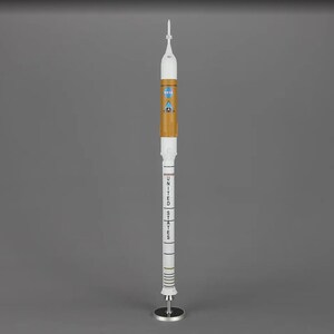 May include: A white model rocket with a brown and orange body, a white nose cone, and a black and white stripe pattern. The rocket has the text "UNITED STATES" and a NASA logo on the side.