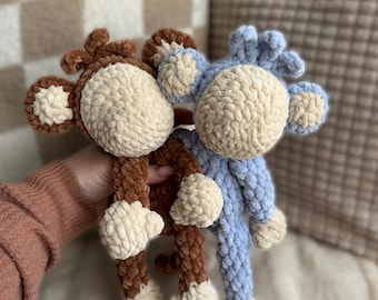 May include: Two plush monkey toys, one brown and one blue, with cream-colored faces, hands, and feet. The toys are made of a soft, textured material. The text "CUDDLY MONKEY MAVERICK PDF PATTERN - SNUGGLER" is at the top.